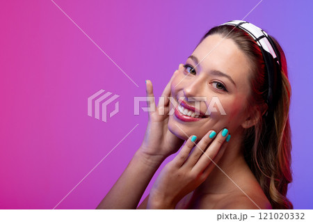 Portrait of caucasian woman wearing blue nail polish on purple background, copy space 121020332