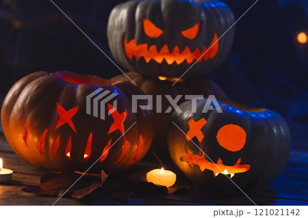 Three carved pumpkins and candle on black background 121021142