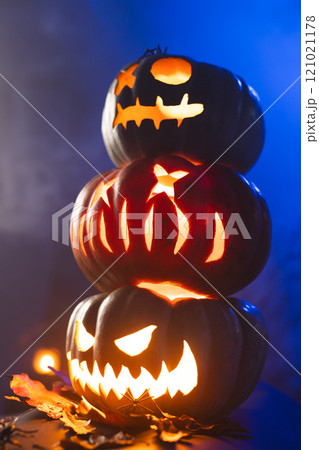 Vertical image of three illuminating carved pumpkins tower on blue background 121021178