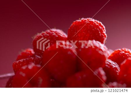 Micro close up of raspberries in glass bowl with copy space on red background 121021474