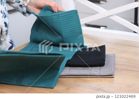 A woman reviews kitchen towels. Three towels of different colors A woman reviews kitchen towels. Three towels of different colors 121022469