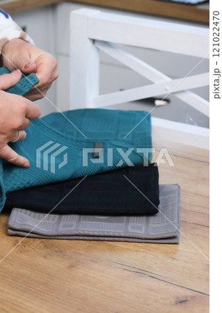 A woman reviews kitchen towels. Three towels of different colors are lying on the table. A woman reviews kitchen towels. Three towels of different colors are lying on the table. 121022470