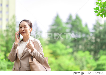 歩きながらスマートフォンで会話するビジネスウーマン 歩きながらスマートフォンで会話するビジネスウーマン 121022963