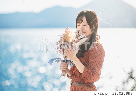 湖でドライフラワーを持って立っている赤いワンピースの女性 121022995