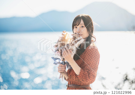 湖でドライフラワーを持って立っている赤いワンピースの女性 121022996