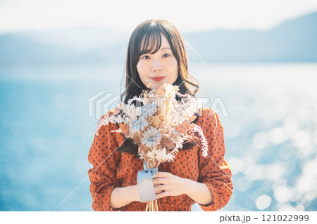 湖でドライフラワーを持って立っている赤いワンピースの女性 121022999