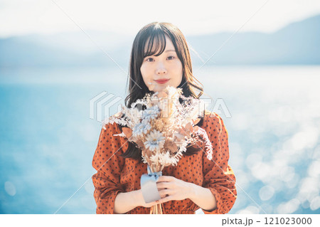 湖でドライフラワーを持って立っている赤いワンピースの女性 121023000