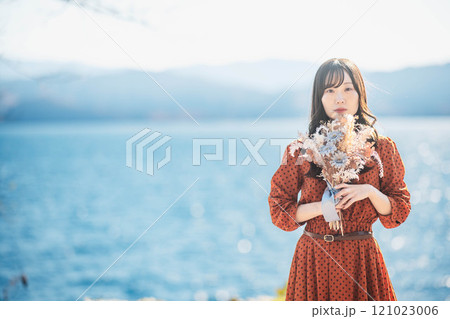 湖でドライフラワーを持って立っている赤いワンピースの女性 121023006