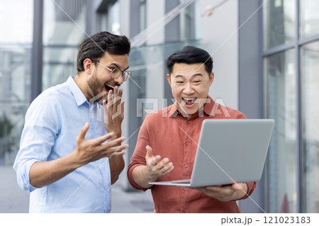 Two ecstatic colleagues celebrate a surprising success while looking at a laptop screen. Their joyous expressions and the laptop highlight a moment of achievement and teamwork. 121023183