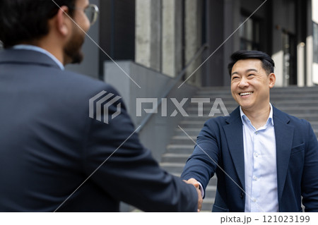 Two business professionals in formal attire shaking hands, symbolizing a successful partnership. The outdoor setting and bright smiles convey trust, connection, and collaboration. Two business professionals in formal attire shaking hands, symbolizing a successful partnership. The outdoor setting and bright smiles convey trust, connection, and collaboration. 121023199