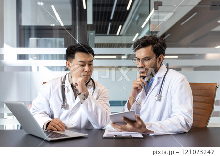 Two doctors engage in medical discussion, using laptop and tablet, in office. Concept of technology, collaboration, consultation. Stethoscope, healthcare professionals, teamwork, medical discussion. Two doctors engage in medical discussion, using laptop and tablet, in office. Concept of technology, collaboration, consultation. Stethoscope, healthcare professionals, teamwork, medical discussion. 121023247