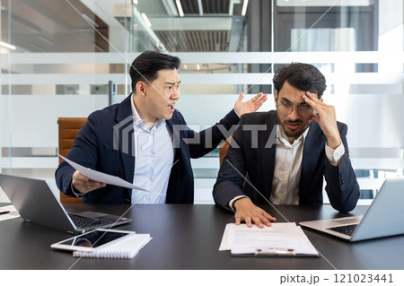 Angry colleague yelling at a stressed employee in a modern office setting. This scene captures workplace conflict, frustration, and pressure as they engage in a heated discussion over paperwork. 121023441