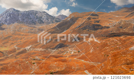 Autumn mountain landscape with golden slopes, rocky peaks, and a clear blue sky 121023698
