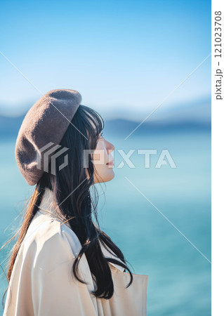 青空をバックにしたベレー帽をかぶりトレンチコートを着た若い女性 121023708
