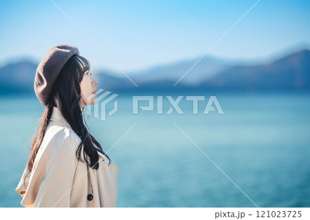 青空をバックにしたベレー帽をかぶりトレンチコートを着た若い女性 121023725