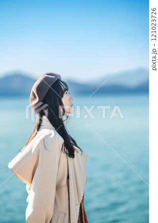 青空をバックにしたベレー帽をかぶりトレンチコートを着た若い女性 121023726