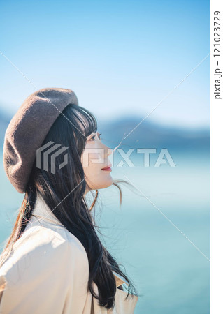 青空をバックにしたベレー帽をかぶりトレンチコートを着た若い女性 121023729