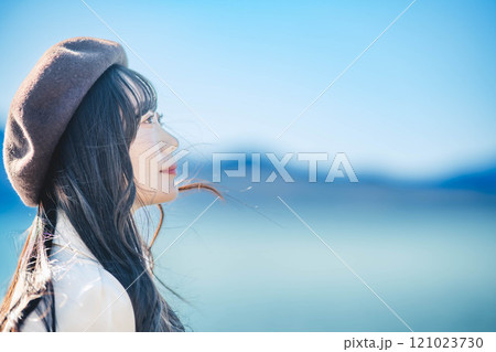 青空をバックにしたベレー帽をかぶりトレンチコートを着た若い女性 121023730