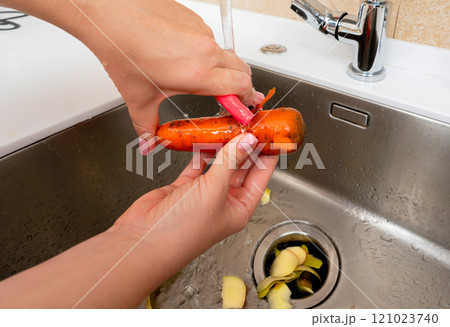 Peeling a carrot over the kitchen sink with running water and waste disposal. 121023740