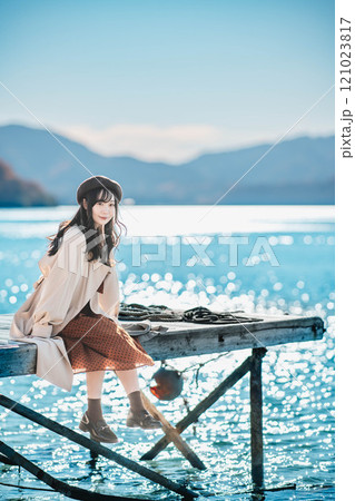 湖の辺りに座るベレー帽とトレンチコートの若い女性 湖の辺りに座るベレー帽とトレンチコートの若い女性 121023817
