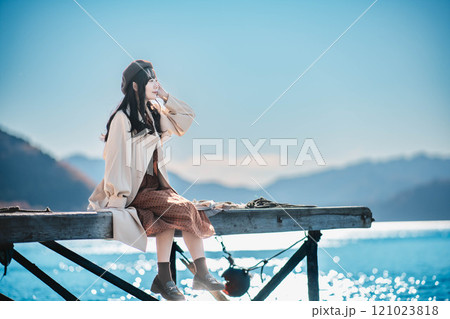 湖の辺りに座るベレー帽とトレンチコートの若い女性 湖の辺りに座るベレー帽とトレンチコートの若い女性 121023818