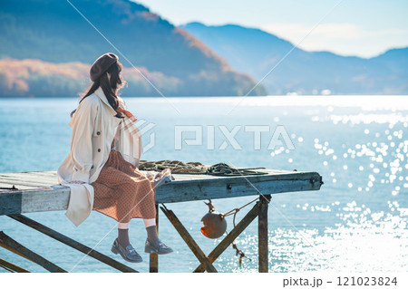 湖の辺りに座るベレー帽とトレンチコートの若い女性 湖の辺りに座るベレー帽とトレンチコートの若い女性 121023824
