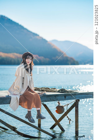 湖の辺りに座るベレー帽とトレンチコートの若い女性 121023825