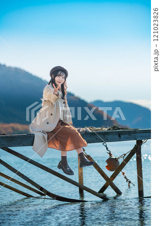 湖の辺りに座るベレー帽とトレンチコートの若い女性 湖の辺りに座るベレー帽とトレンチコートの若い女性 121023826