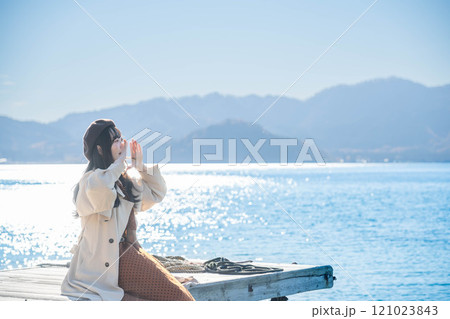 湖の辺りに座るベレー帽とトレンチコートの若い女性 湖の辺りに座るベレー帽とトレンチコートの若い女性 121023843
