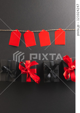 Vertical image of red gift tags on pegs and black gift boxes with copy space over black background Vertical image of red gift tags on pegs and black gift boxes with copy space over black background 121024247