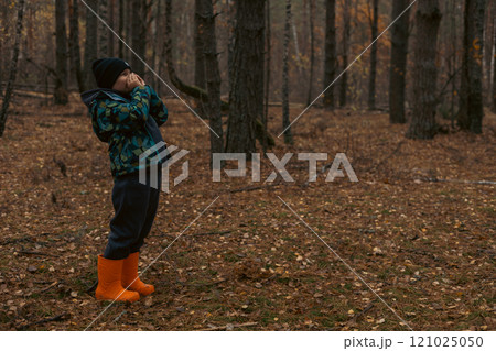 A lost child in orange boots and a warm jacket screams for help in a deserted autumn forest with his hands clasped around his mouth. The child decided to take a walk alone in the forest and got lost. 121025050