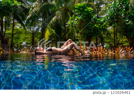 Enjoy a delightful experience of relaxing in a tropical pool surrounded by swaying palm trees Enjoy a delightful experience of relaxing in a tropical pool surrounded by swaying palm trees 121026461