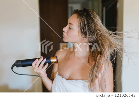 Young woman drying her hair with a styler, a hair dryer at home Young woman drying her hair with a styler, a hair dryer at home 121026545