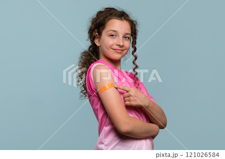 Girl pointing at orange bandage on arm after vaccination 121026584