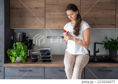 Young woman with healthy diet plan for weight loss, delivery of daily ready meal menu. Food ordered with mobile phone app. Balanced portion with dish. Pre-cooking. 121026877