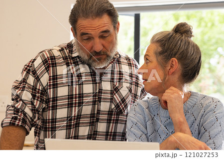 Mature couple discussing plans at home, looking at laptop screen together Mature couple discussing plans at home, looking at laptop screen together 121027253