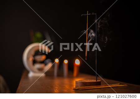 incense stick smokes on a wooden stand on a dark background. Aromatherapy, Smoke while burning incense. smoke for prayers and meditation. prayer to buddha. incense for relaxation and yoga incense stick smokes on a wooden stand on a dark background. Aromatherapy, Smoke while burning incense. smoke for prayers and meditation. prayer to buddha. incense for relaxation and yoga 121027600