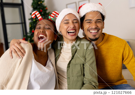 Young multiracial friends wearing festive hats laughing together at home during Christmas 121027666