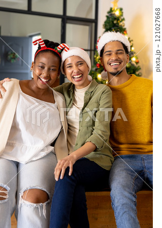 Young multiracial friends wearing festive hats smiling together by Christmas tree at home 121027668