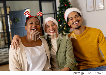 Young multiracial friends wearing festive hats smiling together by Christmas tree at home 121027673