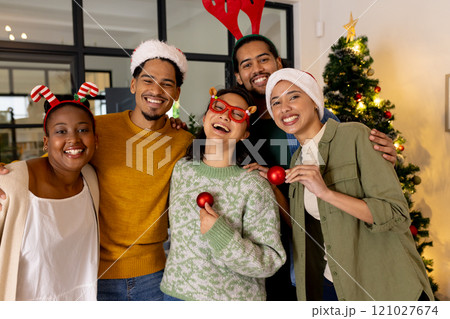 Young multiracial friends celebrating Christmas at home, smiling with festive hats and ornaments Young multiracial friends celebrating Christmas at home, smiling with festive hats and ornaments 121027674