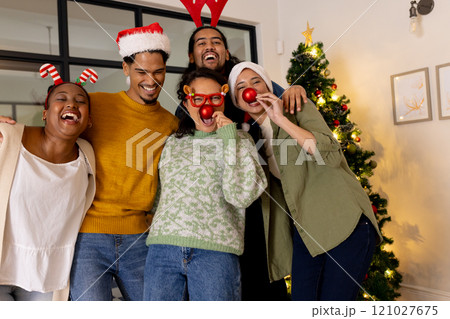 Young multiracial friends celebrating Christmas at home, wearing festive hats and laughing 121027675