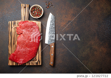 Raw uncooked top round beef steak on wooden cutting board with big kitchen knife and pepper on dark brown rustic stone background top view, cooking meat steak with copy space Raw uncooked top round beef steak on wooden cutting board with big kitchen knife and pepper on dark brown rustic stone background top view, cooking meat steak with copy space 121027722