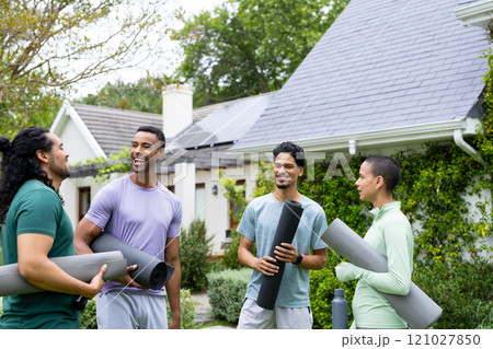 Young multiracial friends laughing and holding yoga mats outside house with solar panels 121027850
