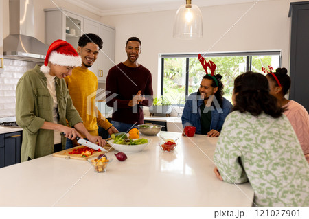 Christmas time, multiracial friends in kitchen preparing holiday meal, wearing festive hats, at home Christmas time, multiracial friends in kitchen preparing holiday meal, wearing festive hats, at home 121027901