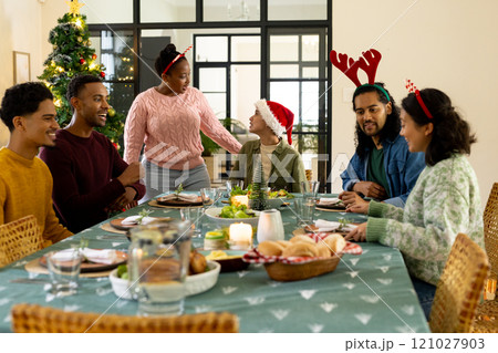 Celebrating christmas dinner, multiracial friends wearing festive hats at home Celebrating christmas dinner, multiracial friends wearing festive hats at home 121027903