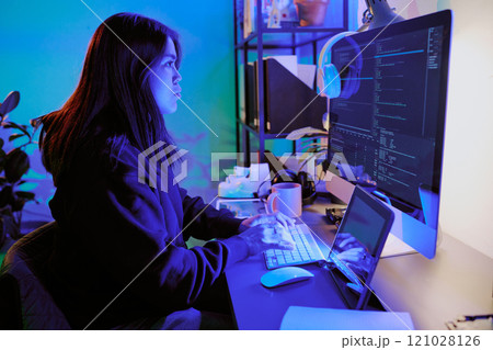 Side view shot of female hacking computer while sitting in dimly lit room by neon lights 121028126