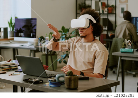 Men with VR headset testing new application and gesticulating wildly while sitting at work desk in office Men with VR headset testing new application and gesticulating wildly while sitting at work desk in office 121028283