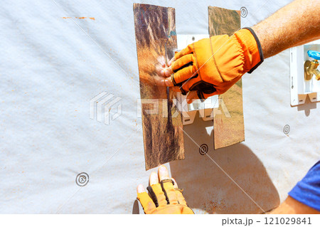 Hands of worker using gloves to install insulation material on wall in a construction area 121029841
