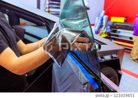 Worker technician applies window tint film to vehicle in workshop setting, focusing on precision quality. 121029851